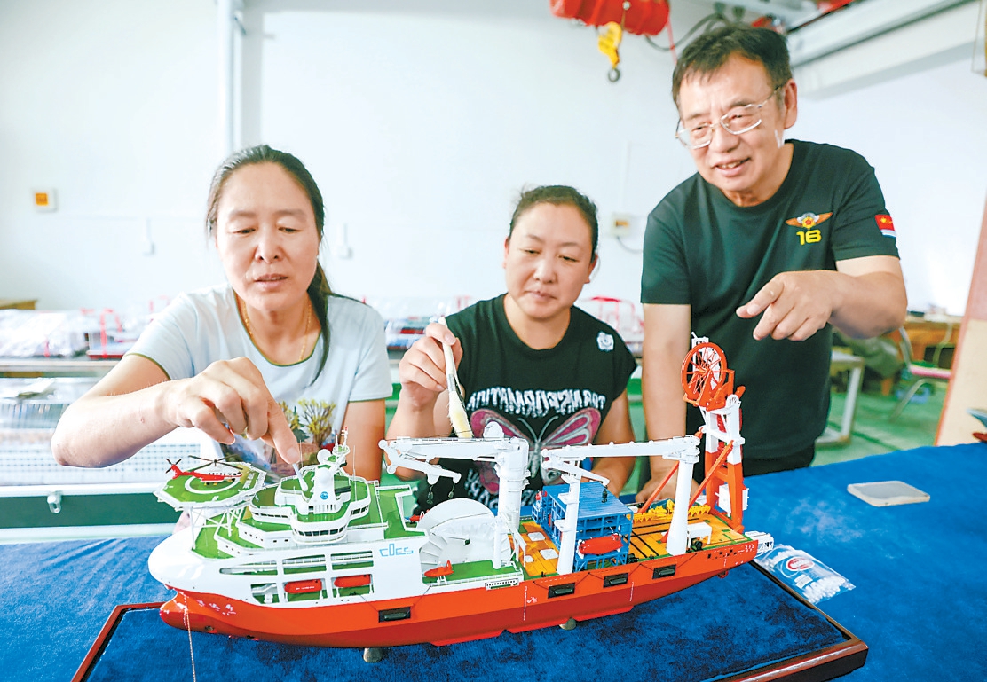 万晓笠（右一）与工人正在整理一艘船模。 本报记者 邓伟摄