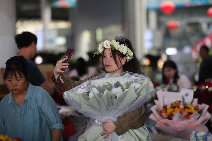 昆明斗南花卉交易市场内，游客正在抱着花束拍照打卡。供图